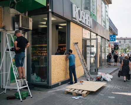 Men place large wooden boards over a shop’s smashed windows as pedestrians walk past