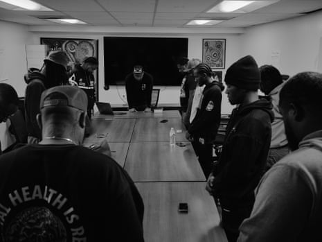 Members of a men’s mental health group stand in a circle around a table and bow their heads in prayer