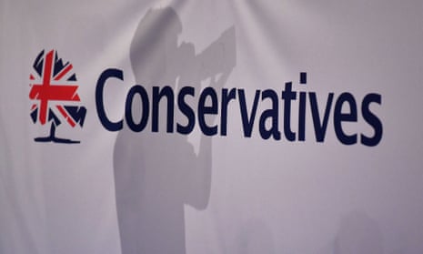 A photographer is seen against the background of a Conservative party banner