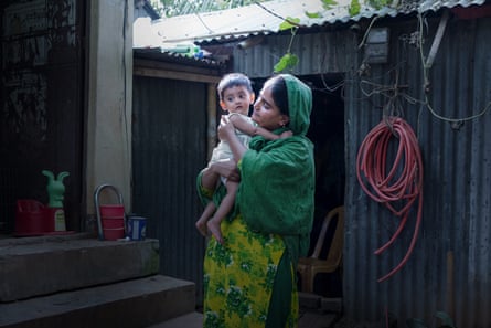 زنی نوزادی را در حیاطی که با کلبه های آهنی راه راه احاطه شده است در آغوش گرفته است