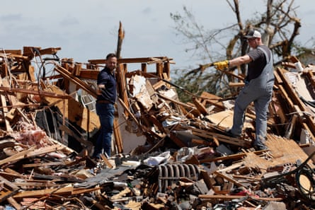 two men stand in piles of rubble outside after tornado