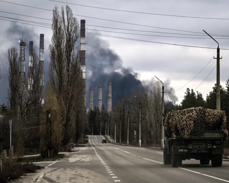 A military vehicle drives on a road as smoke rises from a power plant after shelling outside the town of Schastia, near the eastern Ukraine city of Lugansk.
