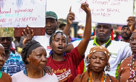 A crowd of protesters with older African women at the front and young people behind them holding placards saying ‘our grabbed land’ and ‘down with brutal monarch’ and references to an anti-colonial leader, Kimathi. 