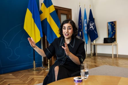 Simona Mohamsson in a meeting room in Stockholm; she sits in front of Swedish, EU, UN, Ukrainian and Nato flags and a blue screen.