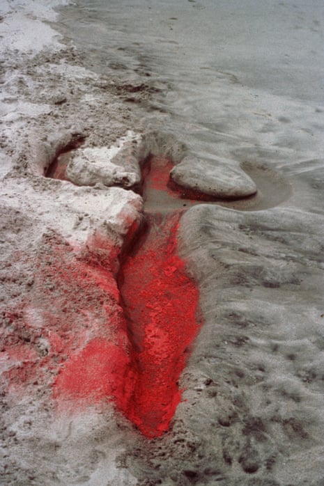 A body-shaped impression carved into beach sand with bright red pigment filling the form