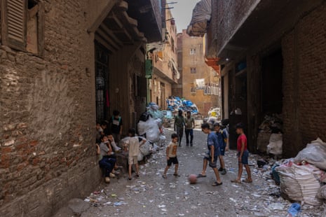 A group of children kick a football in a street lined with bags of rubbish