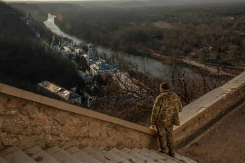 A person wearing fatigues looks down at a river from a Soviet war memorial