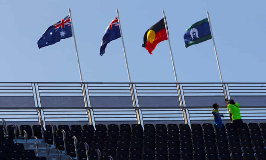 Workers raise the flag of the Torres Strait Islands next to an Australian Aboriginal flag, the Queensland state flag and the Australian national flag on a stand above the Commonwealth Games competition swimming pool on the Gold Coas