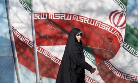 An Iranian woman walks next to a wall painting of Iran’s national flag on a street in Tehran