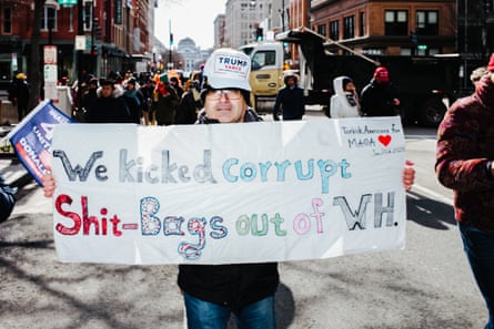 a man carrying a sign that says “we kicked corrupt shit-bags out of WH”