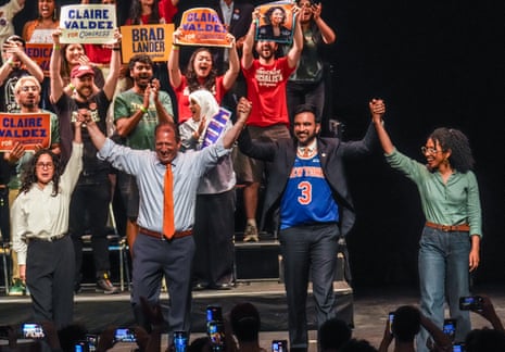 four people stand on stage holding hands as people surrounding them cheer