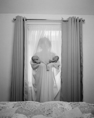 Black and white photograph of a woman behind a net curtain, holding two babies in each of her arms.
