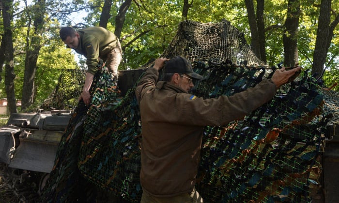 Ukrainian service members cover a tank with a camouflage net at their position in the Kharkiv region