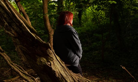 A woman with red hair standing behind a tree with her back towards the camera