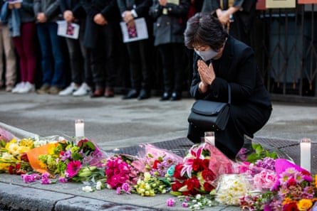 woman kneels with hands pressed together in front of flowers