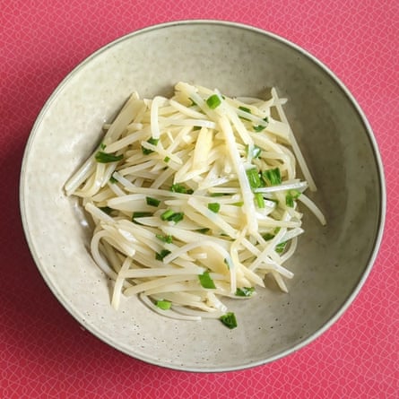 A bowl of julienned potato garnished with sliced spring onions.