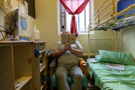 A man sitting in a prison cell reading a book.