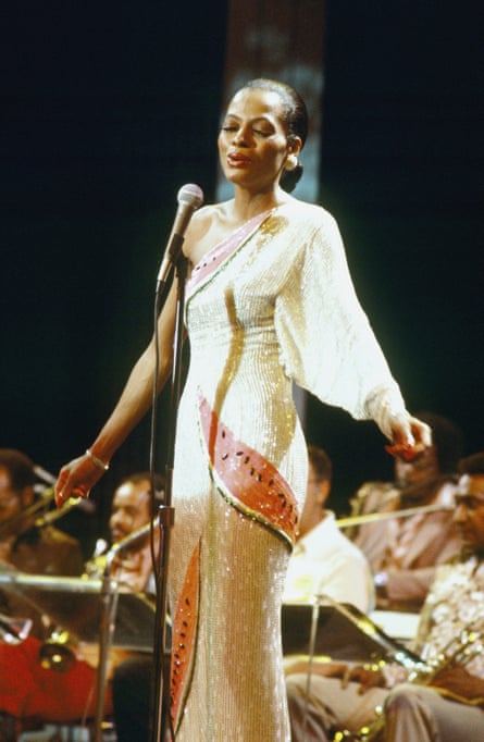 A woman with scraped back hair wearing a tight fitting sparkly one shouldered evening dress singing