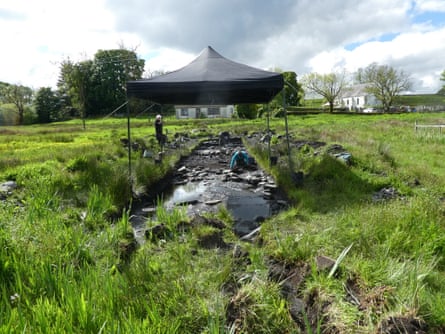 View across a grassy field with a canvas gazebo over an area that is being excavated.