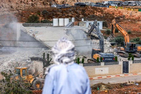A Palestinian man watches as Israeli bulldozers demolish the Palestinian building.