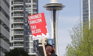 A protester carries a sign that reads “Unionize Amazon Tax Bezos,” in reference to Amazon founder and CEO Jeff Bezos, while riding a bike during a car-based protest at the Amazon Spheres in downtown Seattle.