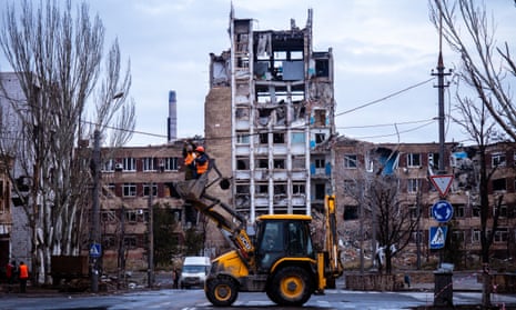 Workers repair a power line in front of a damaged building in Mariupol.