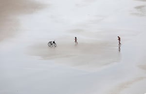 A girl runs towards her bicycle, accompanied by a relative, on a beach in Guaruja.