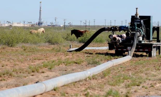 Large hoses lead from one hydraulic fracking drill site to another as horses graze in a Midland, Texas, field. 