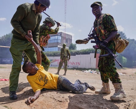 Man on ground with three police over him, one holding his arm and the other with a raised stick