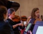 Two women play violins while reading from music stands in a performance setting