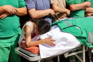 A girl weeps over a white body bag draped in a green paramedic's vest