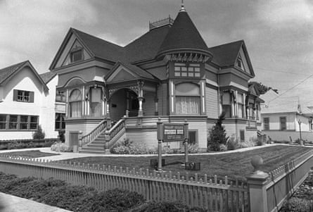 A black-and-white photo of a turreted, three-story Victorian on a corner, bordered by a low iron fence.