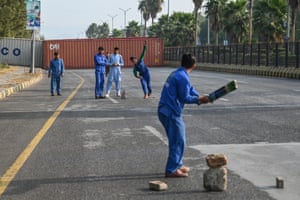 Workers play cricket on a deserted road blocked with shipping containers