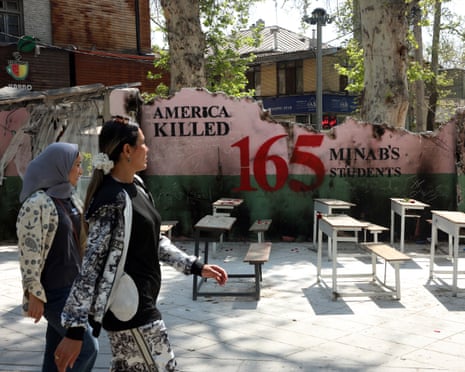 Women walk past a mural referring to the Minab school bombing in Tehran