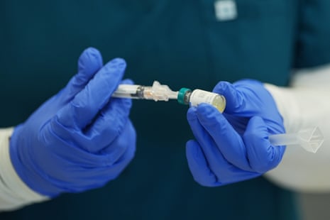 Gloved hands prepare a measles, mumps and rubella vaccine, connecting syringe and vial