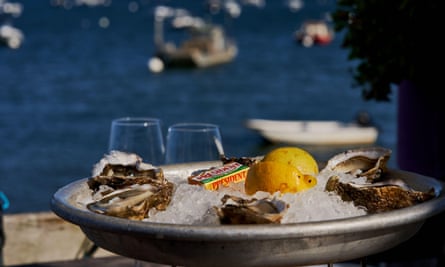 Arcachon bay with fishing and sailing vessels in the background with oysters served on a bed of ice with butter, lemon and wine glasses in the front