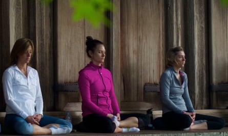 Three women sitting in a row, cross-legged on the ground, meditating