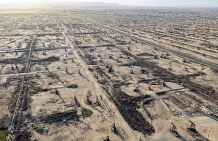 An aerial photo showing large dusty field filled with oil pumpjacks stretching into the distance