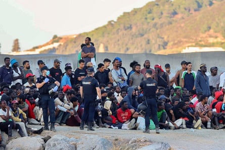 Police officers guarding migrants by the sea at Ceuta in Spain.