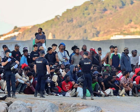 Police officers guard a group of migrants at El Trampolin beach in Ceuta, Spain.