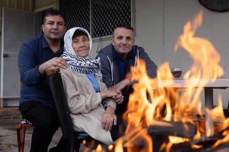 Fatma with two of her sons, Shamikh and Majed, seated in chairs in a back yard with a campfire burning in the foreground
