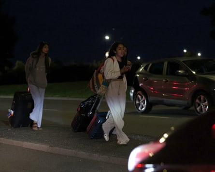 People pulling suitcases beside cars at night