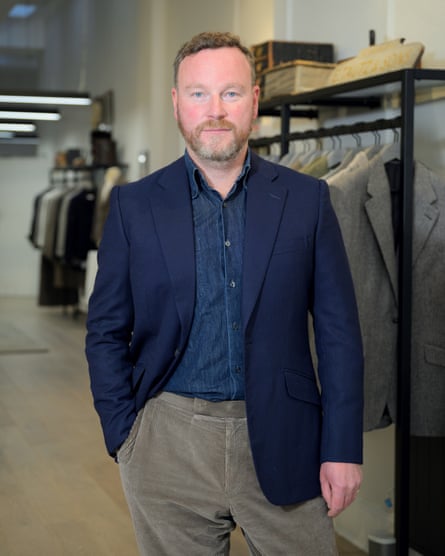 James Sleater in suit jacket and chinos, standing in fronts of suits on rails