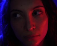 Extreme close-up of a woman's face lit by blue and red light, gazing sideways in horror film Goody Goody