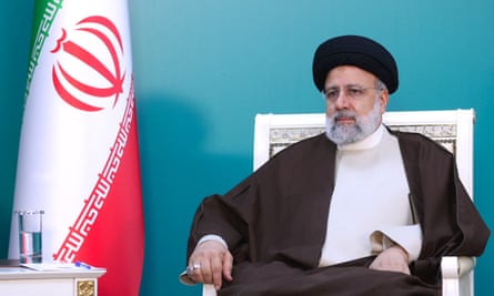 Ebrahim Raisi sits in a chair next to the Iranian flag