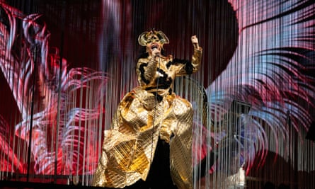 Björk performs on stage wearing elaborate gold headdress, mask and dress