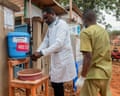 A black doctor in white coat washing his hands in a basic setup during treatment of Ebola patients