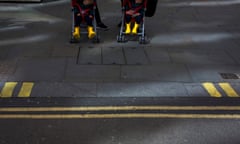 Two small children sleep in their respective buggies as unseen parents prepare to cross a street in the City of London. We see the repetition of yellow bars and parallel lines from the childrens' boots and parking restriction lines on the kerb and road.