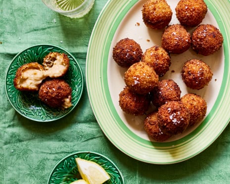 An oval plate on a green cloth, with crab croquetas and lemon garnish