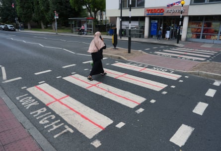 A woman walks across a zebra crossing where red crosses are spray painted on to the white rectangles on the road